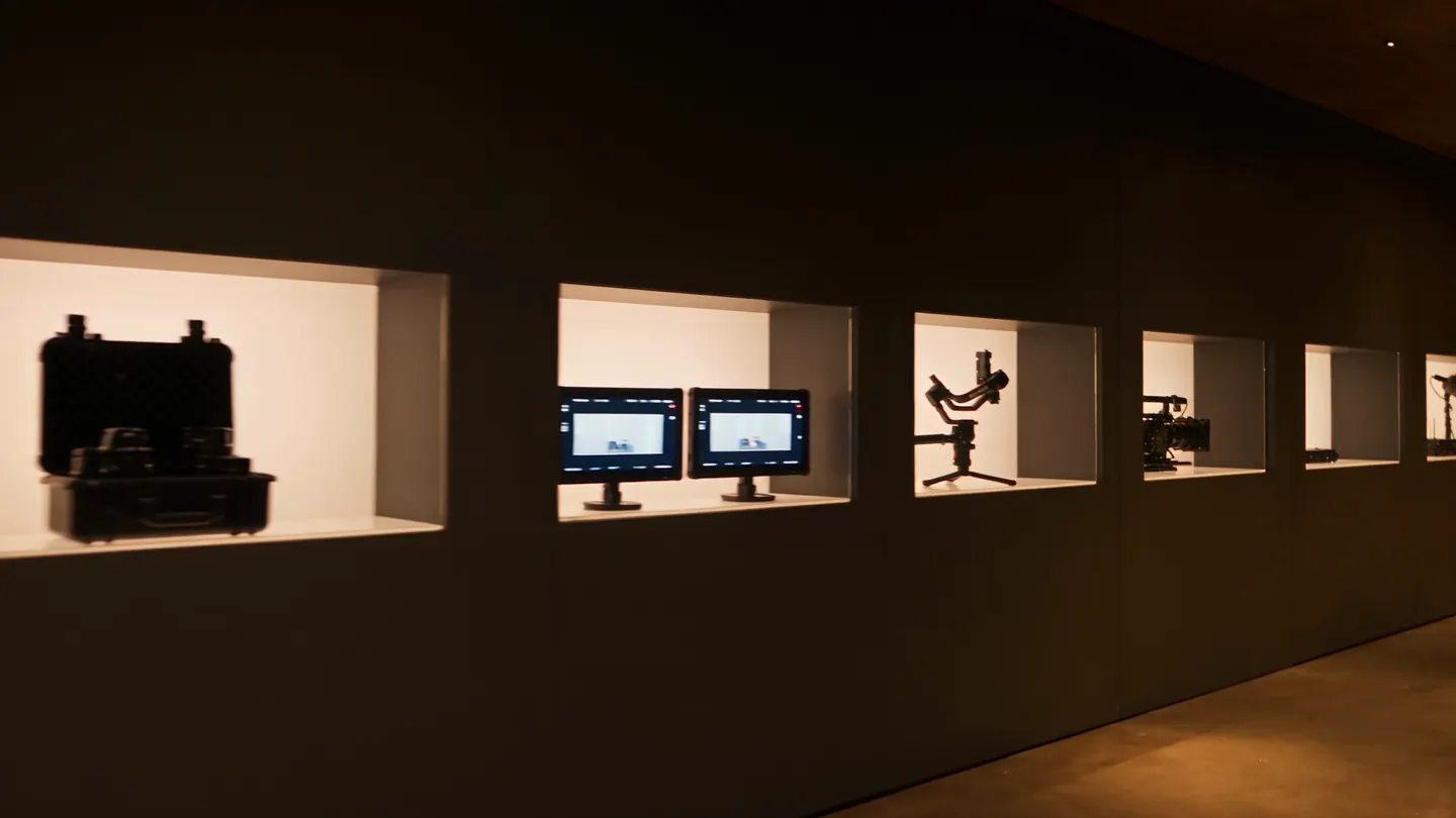 A corridor with five lit display cases: lenses, monitors, a gimbal, a compact camera and a microphone.