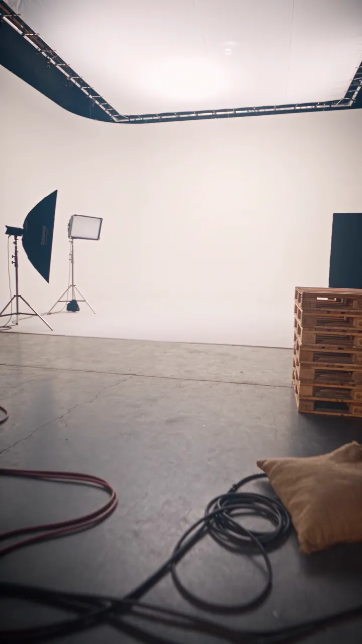 The studio's white cyclorama: a big light frame, a softbox, wooden pallets and cables on the floor.