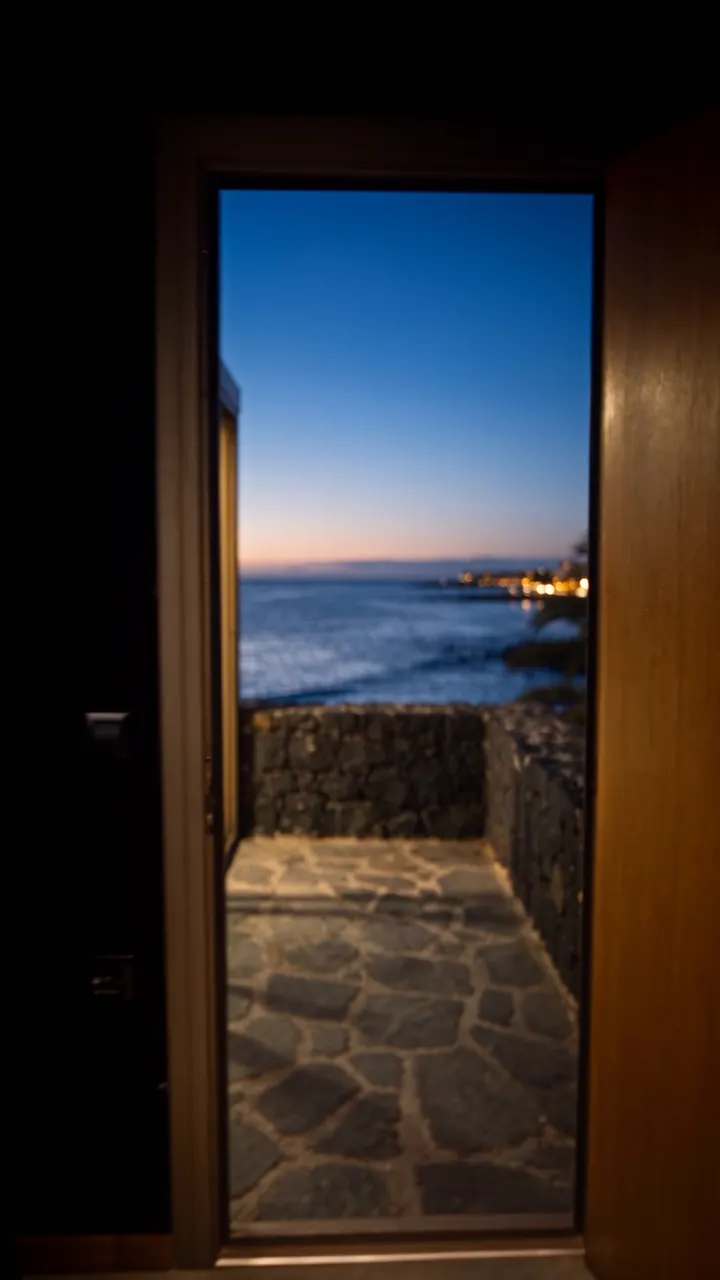 The studio door open onto the terrace: outside, the sea at blue hour.